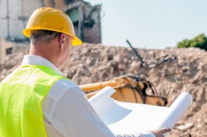 portrait-of-site-manager-posing-with-blueprints-against-unfinished-building_1391-889